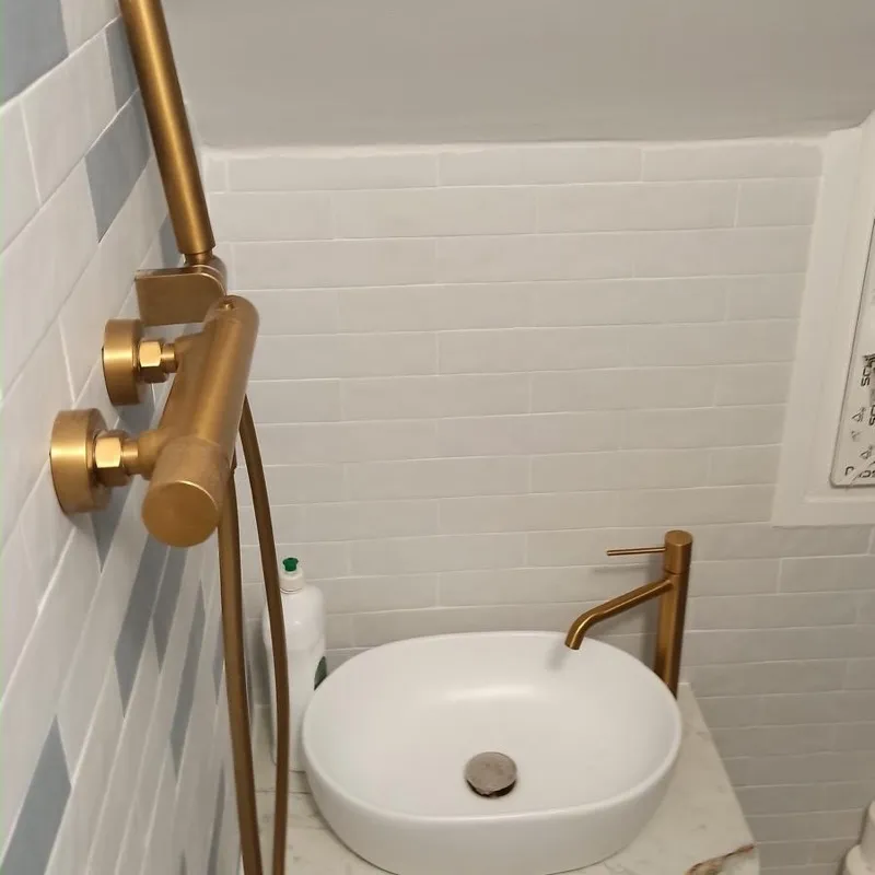 Aseo con columna de ducha y grifo dorados, lavabo sobre encimera y azulejo biselado blanco y azul