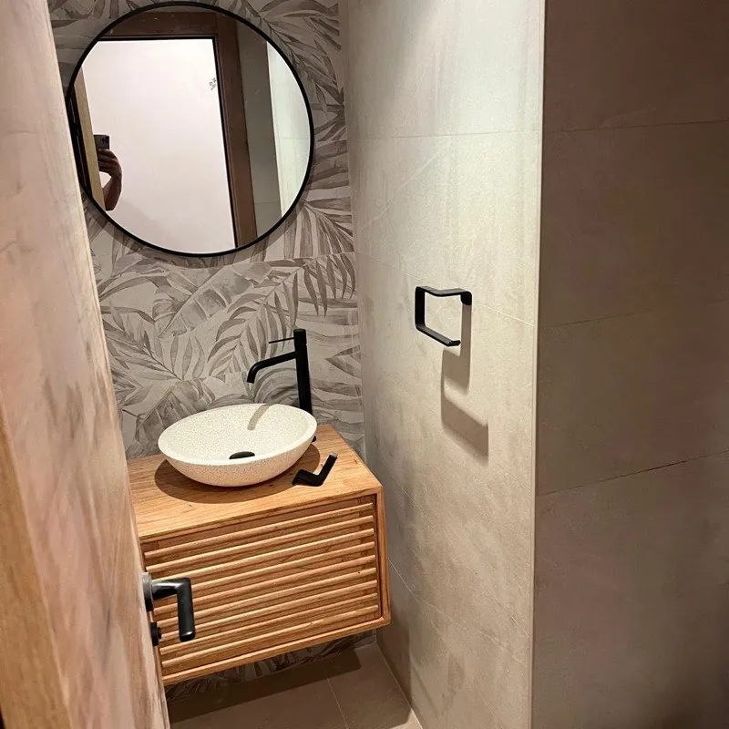 Aseo reformado con papel pintado de palmeras, lavabo blanco y mueble flotante de madera