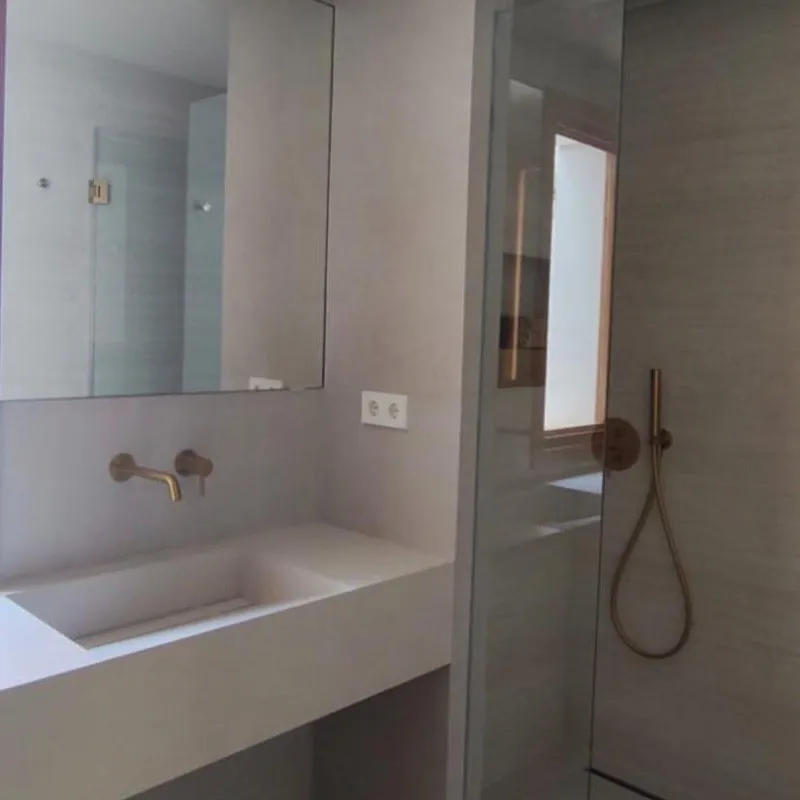 Baño de microcemento con grifería dorada empotrada y ducha de obra