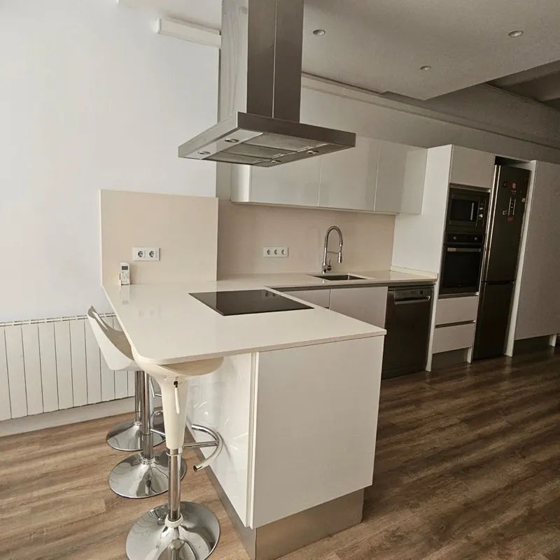 Cocina blanca con península, barra de desayuno con taburetes, campana de isla y suelo laminado