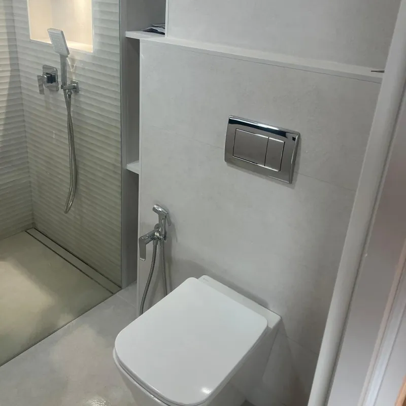 Baño reformado con inodoro suspendido, cisterna empotrada con pulsador cromado y ducha de obra
